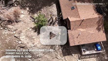 Aerial view of firefighters digging in mud near a house in Forest Falls, CA, with a video play button overlay. Dated September 19, 2025.