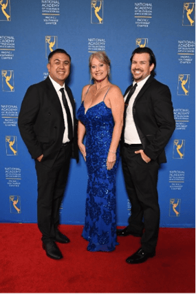Three people pose on a red carpet in formal attire before a National Academy of Television Arts & Sciences backdrop.