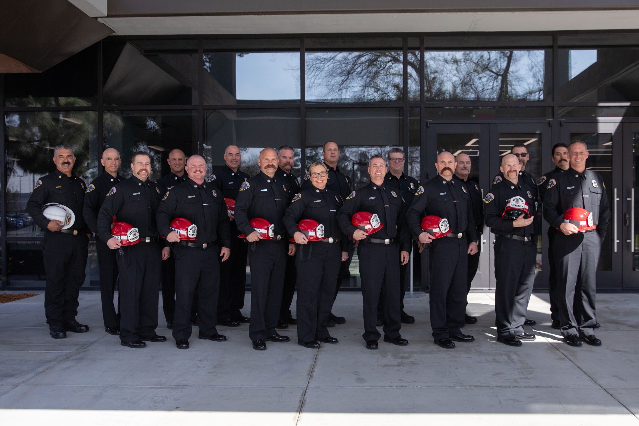 A group of newly promoted County Fire battalion chiefs and captains pose for a photo in front of a building.