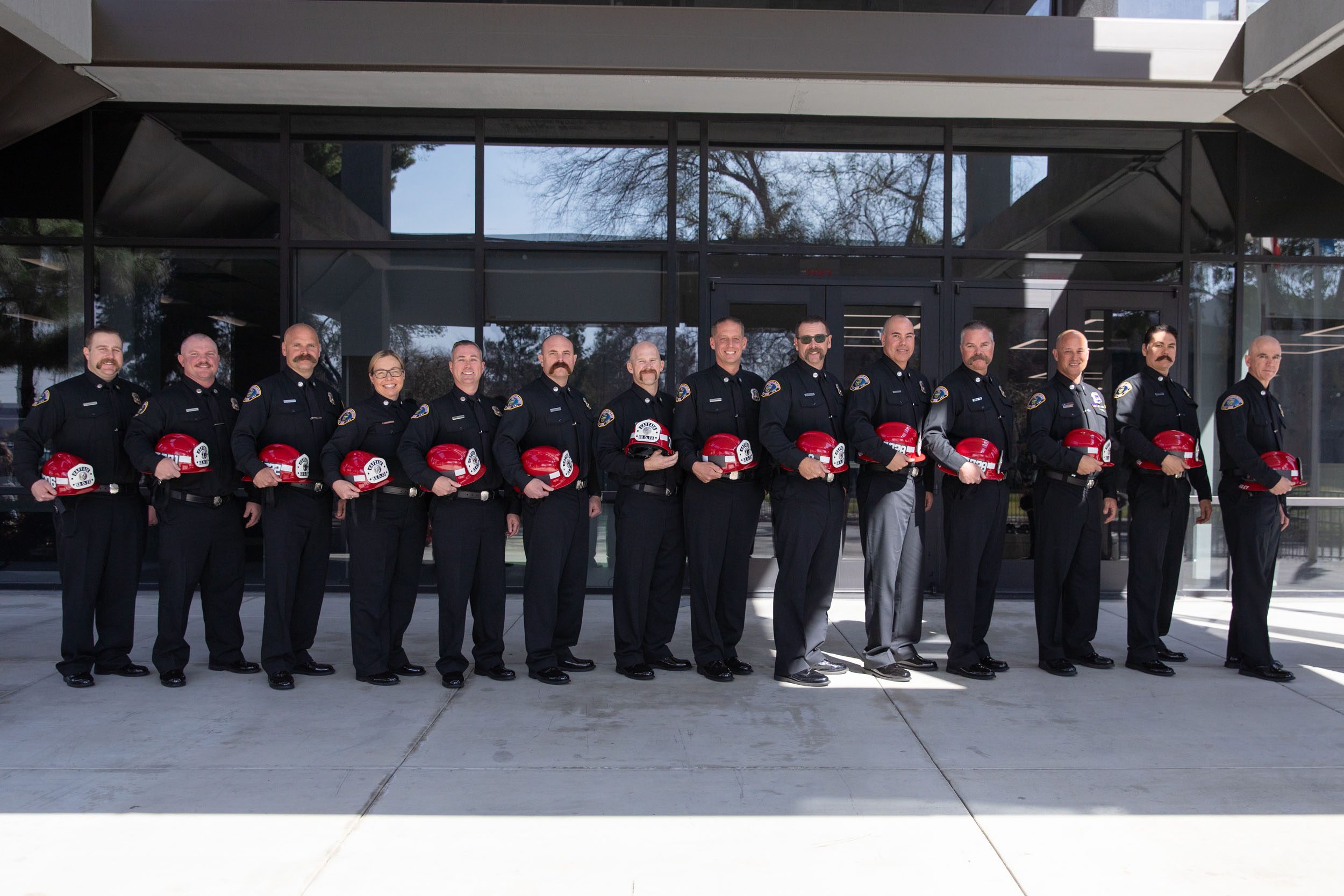 A group of newly promoted County Fire battalion chiefs and captains pose for a photo in front of a building.