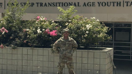 Military man standing in front of bushes and One Stop Transitional Age Youth building.