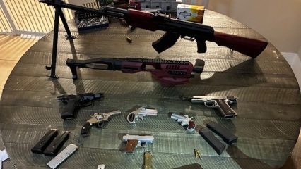 A round wooden table displays various firearms, including rifles, pistols and revolvers, alongside ammunition boxes.