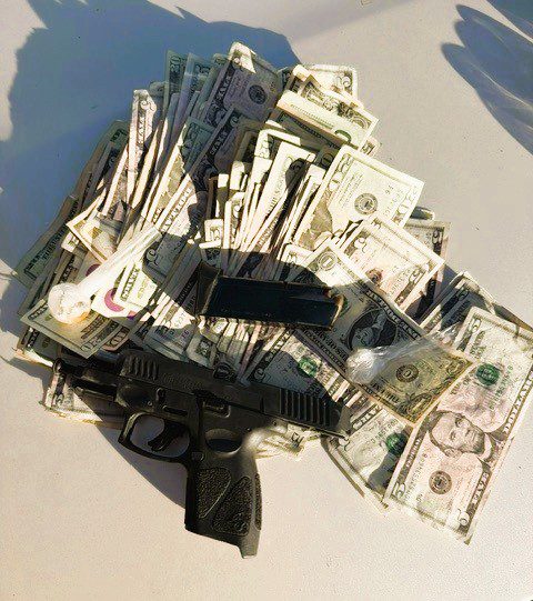 A pile of cash under a disassembled gun on a gray surface.