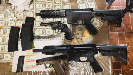 Firearms and accessories are displayed on a table covered with cash.