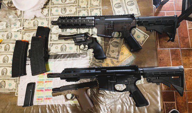 Firearms and accessories are displayed on a table covered with cash.